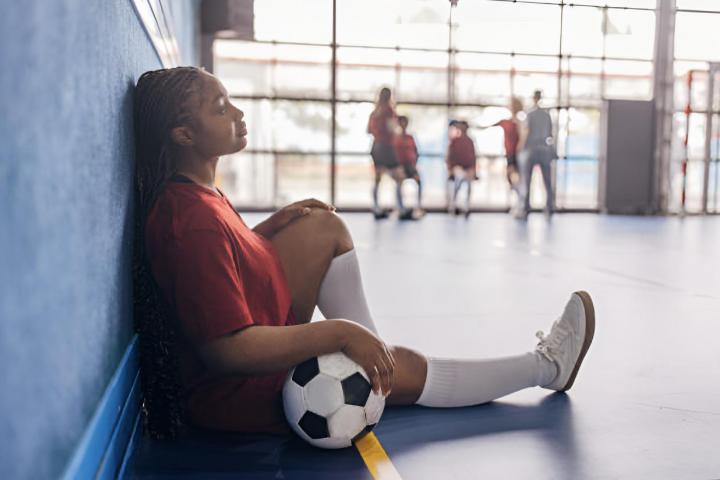 Una joven jugadora de fútbol sentada con la pelota contra la pared azul