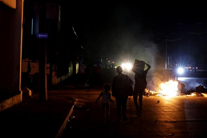 Varias personas caminan junto a basura incendiada en medio de una calle, durante una protesta contra los frecuentes cortes de luz, en La Habana (Cuba), 13 de mayo de 2026.