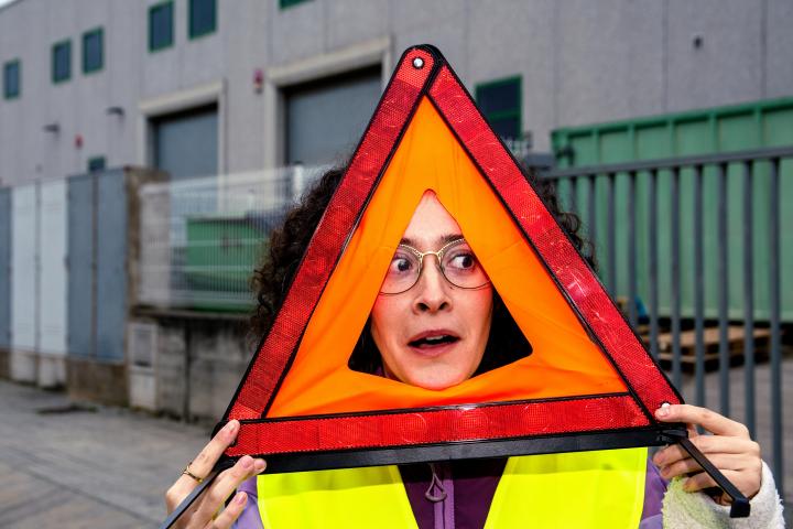 Una persona que lleva puesto un chaleco de seguridad y sostiene un triángulo de emergencia de color rojo brillante y naranja.