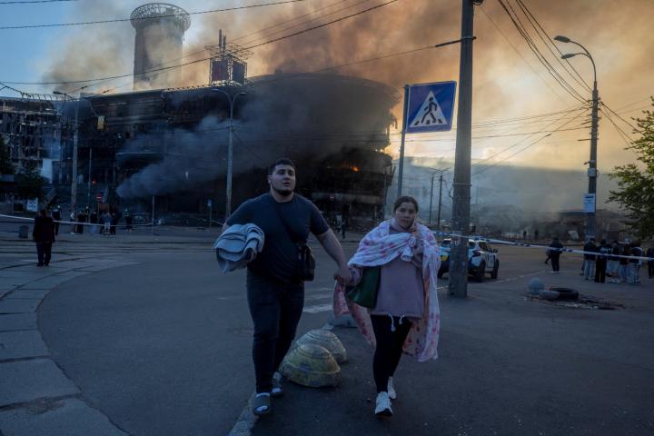 Varias personas caminan cerca de un edificio en llamas, al salir de un refugio tras los ataques nocturnos con misiles y drones rusos, el 24 de mayo de 2026, en Kiev.