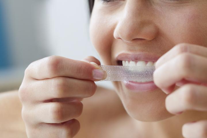 Primer plano de una joven usando una tira blanqueadora de dientes.