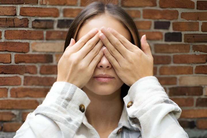 Una chica tapándose los ojos con las manos mientras los cierra