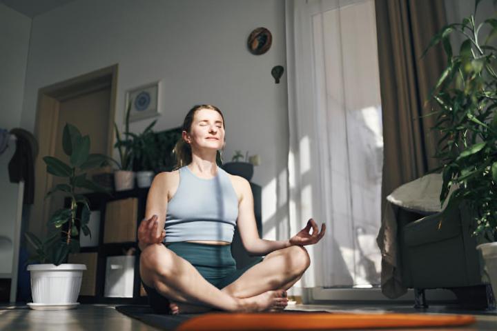Una mujer disfrutando de un momento de paz meditando, arropada por la calidez de su hogar.