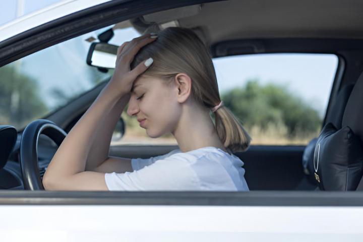 Una mujer frustrada con las manos en la cabeza mientras está sentada en su coche