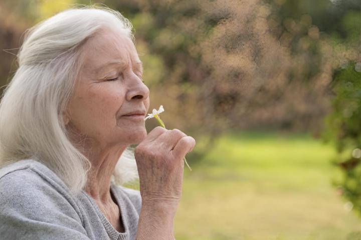Una señora mayor oliendo una flor blanca de su jardín