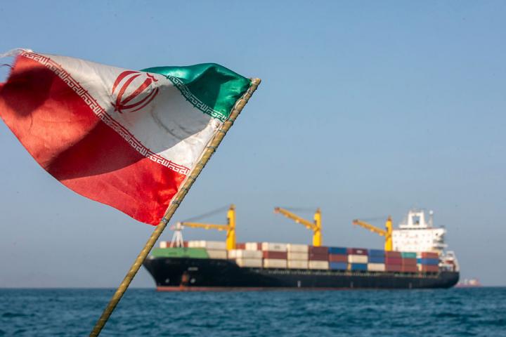 Una bandera iraní ondea al viento mientras varios barcos permanecen anclados, el 16 de mayo de 2026, en el estrecho de Ormuz, cerca de la isla de Larak.