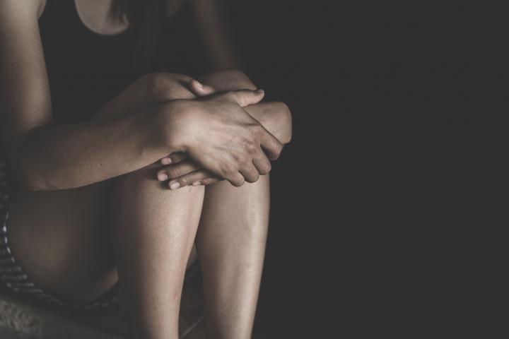 Una mujer abraza sus rodillas con sus brazos, entre las sombras.