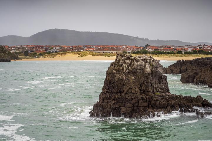Olas rompiendo contra una formación rocosa, con una playa al fondo, en la zona de Arnuero, en Cantabria, en una imagen de archivo.