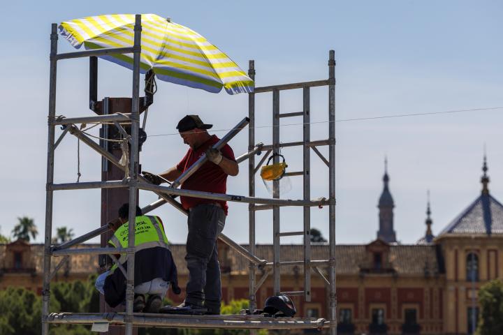 Dos trabajadores se protegen del sol con una sombrilla en el puente de San Telmo en Sevilla.