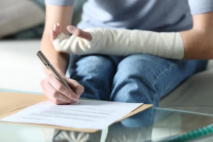 Una mujer con un brazo vendado firmando una baja