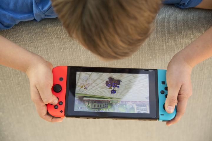 Un niño jugando a la Nintendo Switch: vista cenital, se le ve la coronilla con pelo del niño apoyado sobre un sofá y la Switch encendida