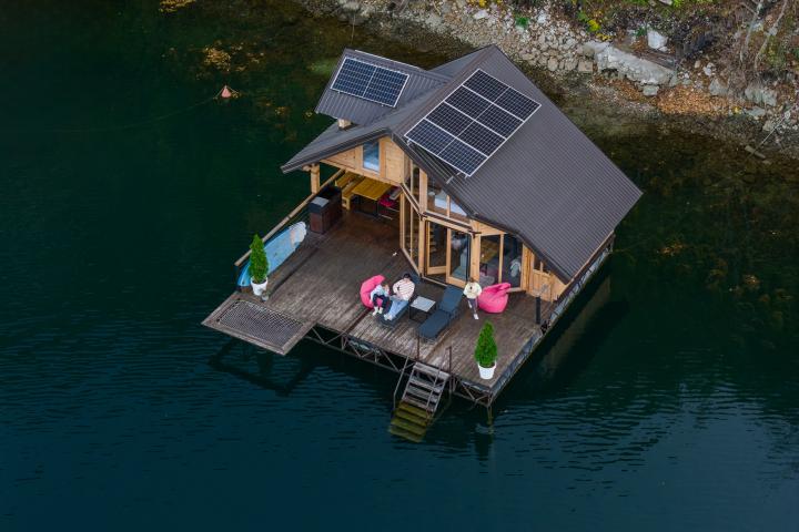Vista aérea de una casa flotante moderna en un lago tranquilo con paneles solares y asientos en la terraza