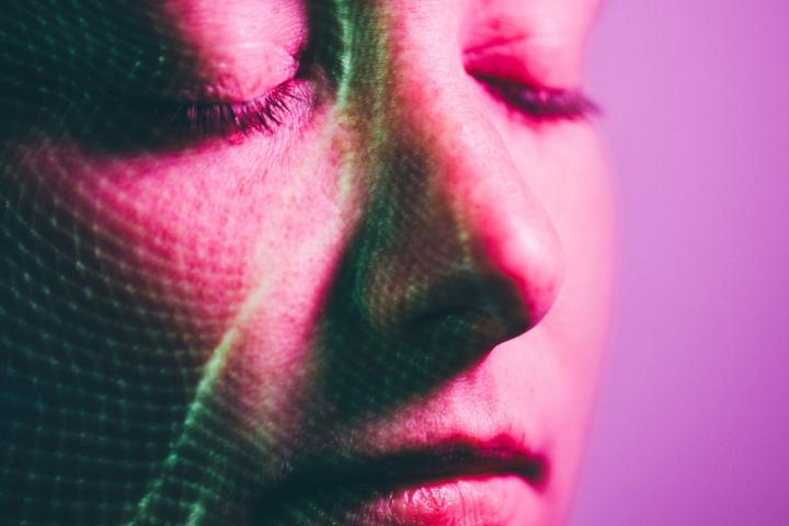 Plano cercano del rostro de una mujer con ojos cerrados en un fondo rosa mientras hay luces verdes iluminándose en su cara