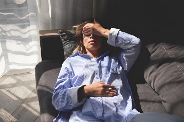Una mujer exhausta por dolor menstrual tumbada en el sofá