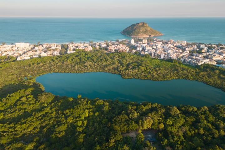 Vista aérea de un lago en un parque y casas frente a la playa con la Roca Pontal en el océano en Río de Janeiro.