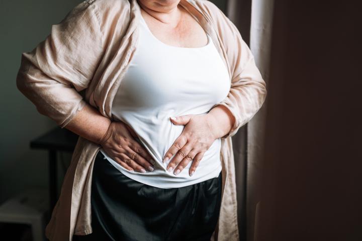 Mujer se presiona las manos sobre la zona del hígado en el abdomen