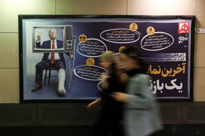 Unas mujeres pasan ante un letrero con una imagen del presidente estadounidense, Donald Trump, herido y con muletas, el 17 de junio de 2026, en Teherán (Irán).