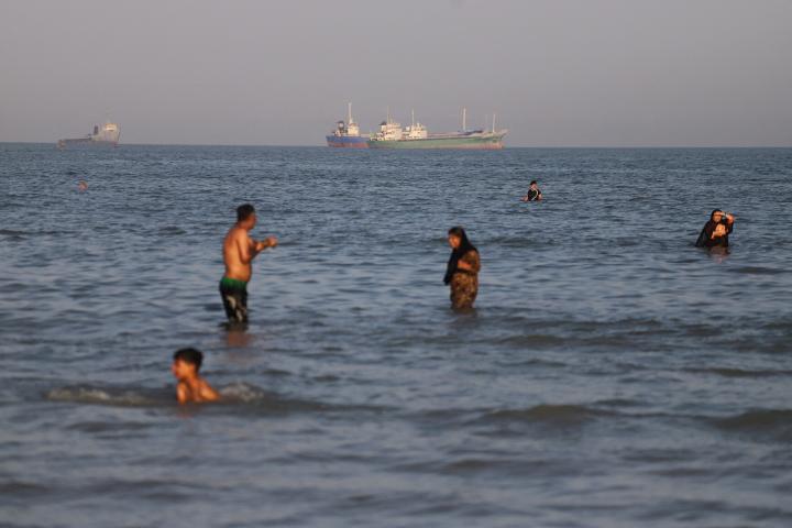 Unos buques, parados en el estrecho de Ormuz, cerca de la playa de Bandar Abbas (Irán), en la que se bañan varias familias, el 17 de junio de 2026.