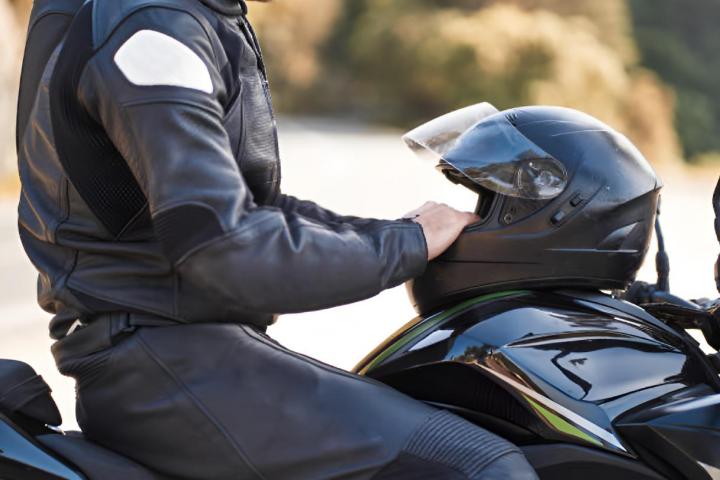 Un hombre sentado en su moto con una chaqueta y un casco de protección.