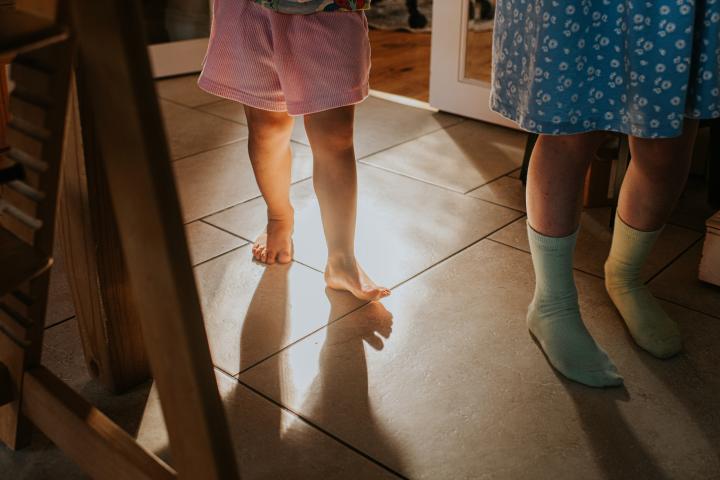 Dos niños pequeños caminan sobre un suelo de baldosas en una habitación. La luz del sol ilumina sus piececitos. Ilustración conceptual con espacio para texto.