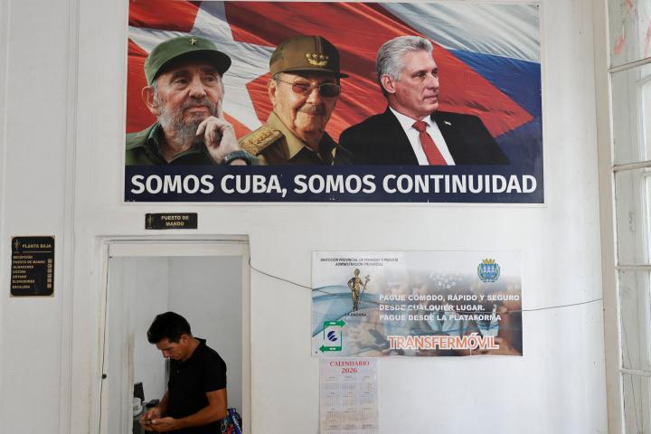 Un hombre revisa su teléfono en una oficina del Ministerio de Hacienda y Precios, bajo un póster de Fidel, Raúl Castro y Miguel Díaz-Canel, el 3 de junio de 2026, en La Habana (Cuba).