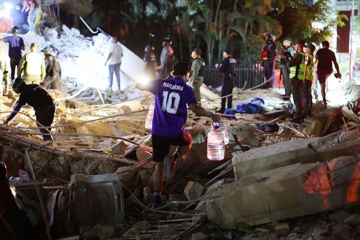 Un hombre con una camiseta de Maradona transporta botellas de agua mientras los bomberos trabajan en un edificio dañado por los terremotos en Caracas (Venezuela), el 24 de junio de 2026.
