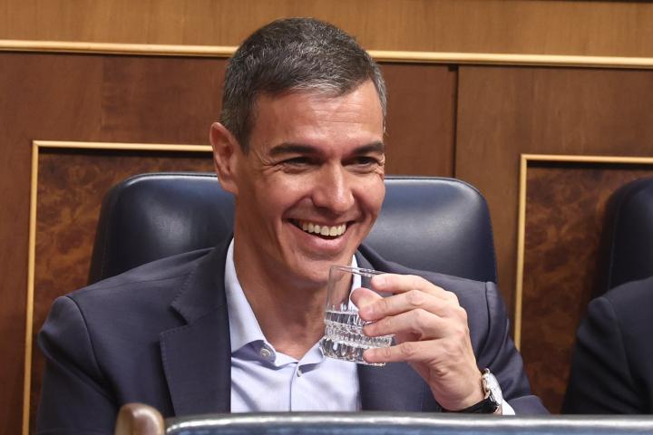 El presidente del Gobierno, Pedro Sánchez, riéndose en el Congreso, con un vaso de agua en la mano.