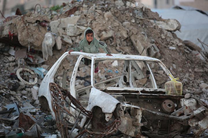Un niño juega sobre un coche destrozado por los ataques de Israel, entre edificios hundidos, en el campo de refugiados de Bureij, en Deir al-Balah (Gaza), el 17 de enero de 2026.