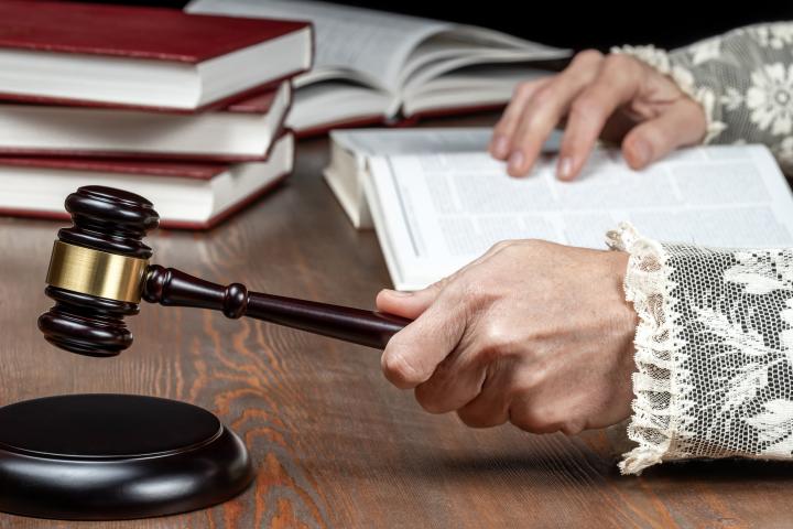 Primer plano de las manos del juez golpeando el mazo, con la toga con puños de encaje y los libros de derecho sobre el escritorio en la sala del tribunal, en una imagen de archivo.