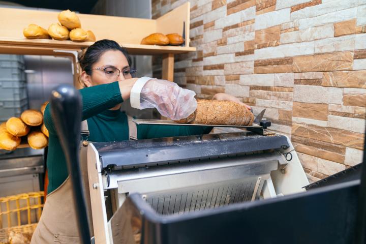 Una panadera usando una máquina para cortar el pan