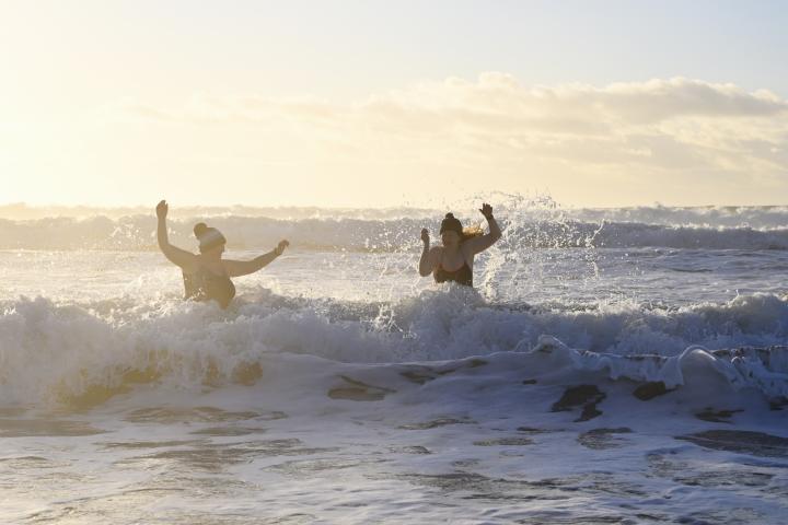 Reino Unido, Cornualles, Kenneck Sands: nadadoras de aguas abiertas saltando al mar al amanecer.