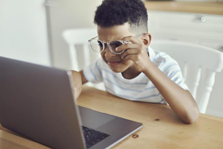 Un niño pequeño con gafas y achinando los ojos para ver mejor la pantalla del ordenador