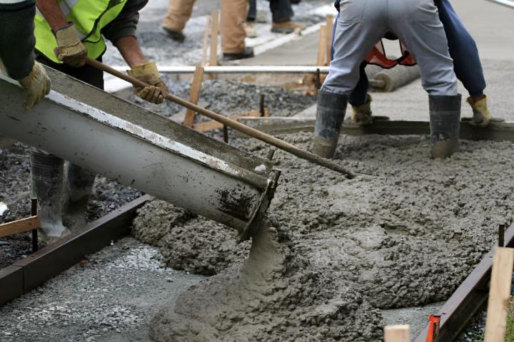 Varios obreros de la construcción alisando el hormigón de la acera.