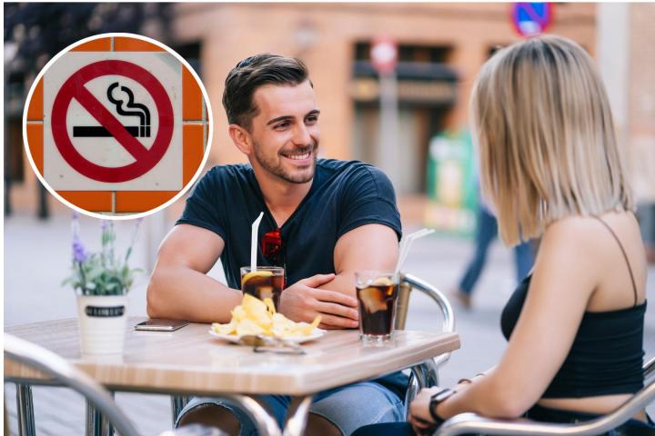 Pareja en una terraza con cartel de prohibido fumar