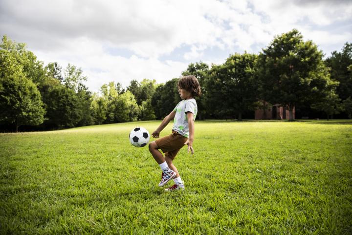 Un niño juega al fútbol en una zona verde.