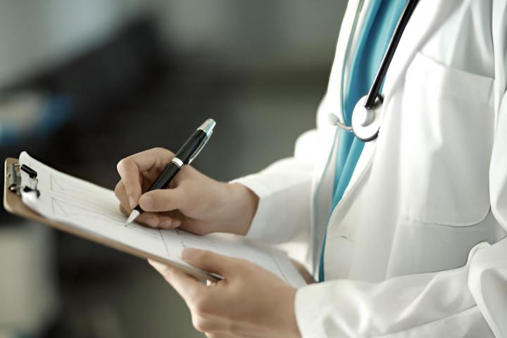 Un médico con estetoscopio anotando síntomas en un papel