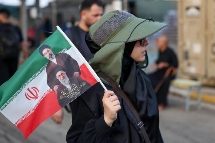 Una peregrina portando una bandera iraní con las fotos de sus líderes supremos llega al paso fronterizo de Mundhiriya camino a Karbala, el 28 de julio de 2026.