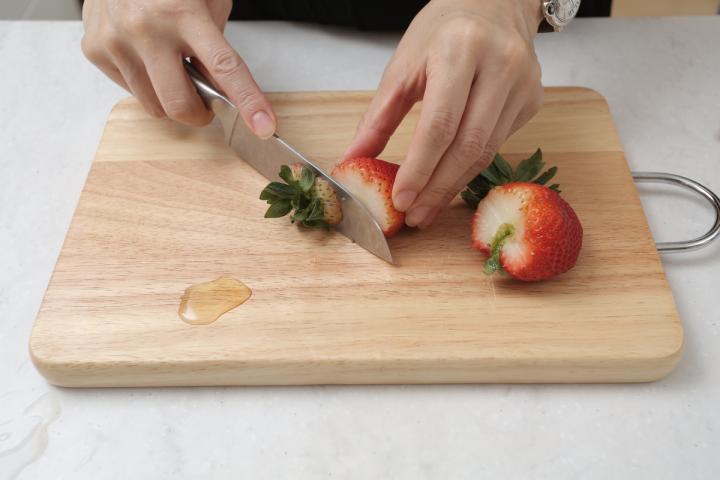 Una persona preparando fresas en una tabla de madera