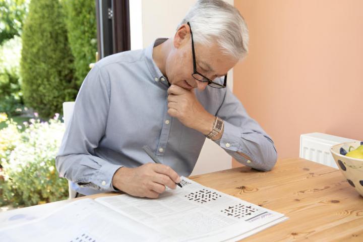 Un señor mayor haciendo un sudoku en una mesa al aire libre