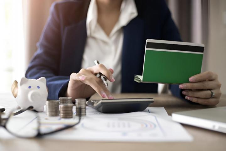 Una mujer haciendo cuentas con una calculadora sobre lo que tiene apuntado en la libreta de ahorros