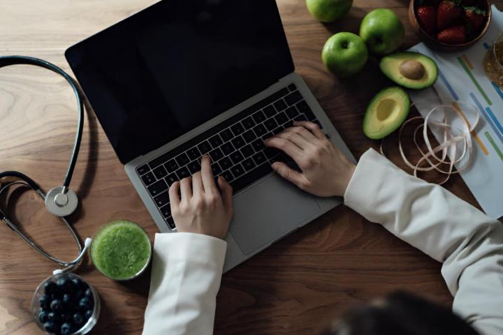 Una vista aéra de una nutricionista trabajando en su ordenador con comida alrededor y un estetoscopio