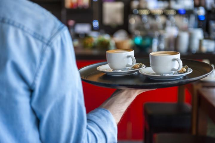 Un camarero, llevando dos cafés en una bandeja.