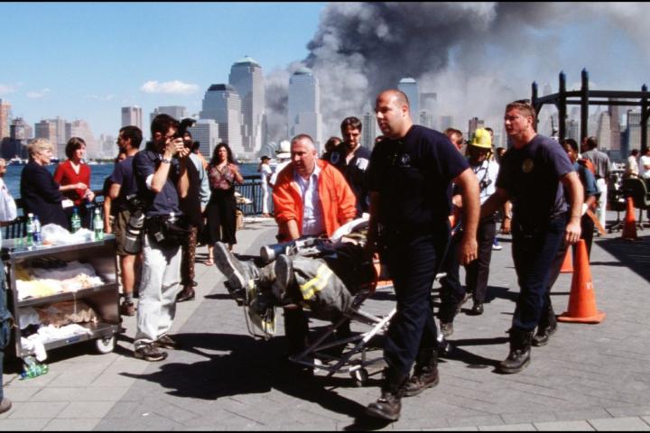 Equipos de emergencia atienden a las primeras víctimas del 11 de septiembre de 2001, con las Torres Gemelas entre humo de fondo.