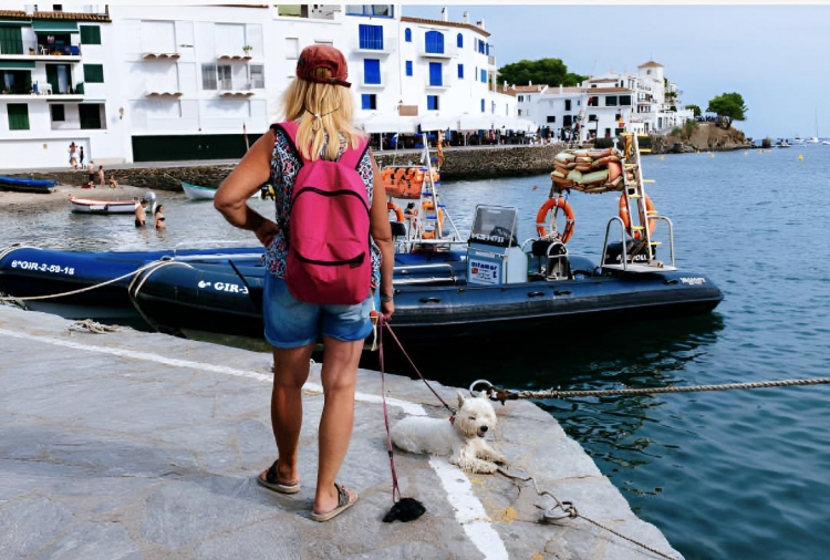 Una mujer paseando con su perro en el puerto de Cadaqués, en Girona