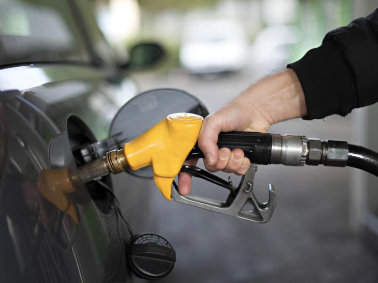 La mano de un hombre echando combustible en su vehículo con una bomba de gasolina amarilla.
