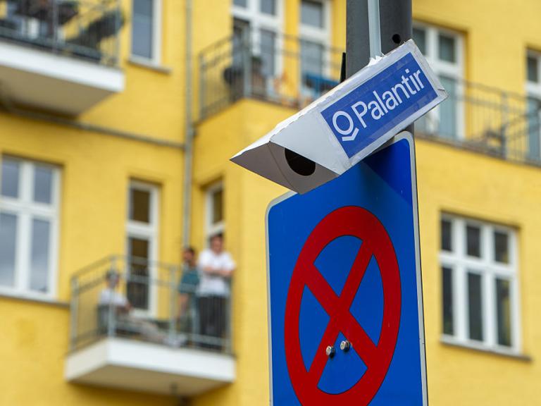 BERLIN, GERMANY - JUNE 13: A false surveillance camera with Palantir written on it attached to a lamp post at the demonstration against the police's expansion of the use of AI (artificial intelligence) powered video surveillance and analysis technology on June 13, 2026 in Berlin, Germany. Amendments to the existing ASOG (General Security and Public Order Act) were passed by the Berlin House of Representatives in December 2025. Civil liberties groups have warned that the amendments lower the thresholds for taking action against individuals and have expressed further concerns that automated facial recognition could lead to mass surveillance of the general public. (Photo by Craig Stennett/Getty Images)