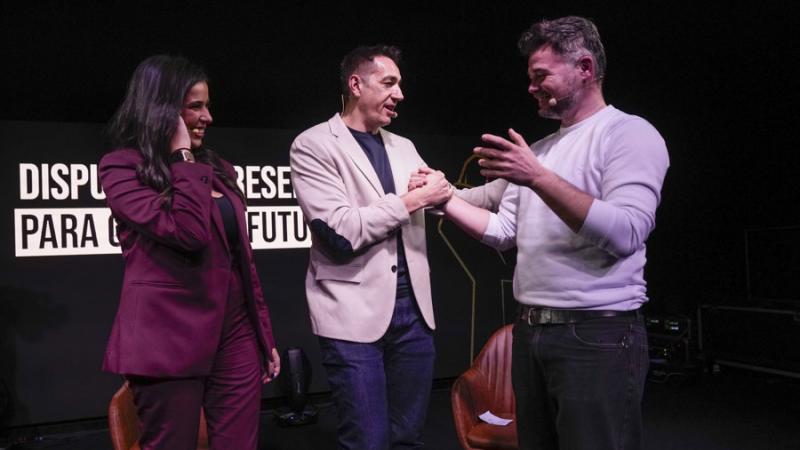Gabriel Rufián y Emilio Delgado se saludan durante su acto por la unidad de la izquierda en presencia de la moderadora, Sarah Santaolalla